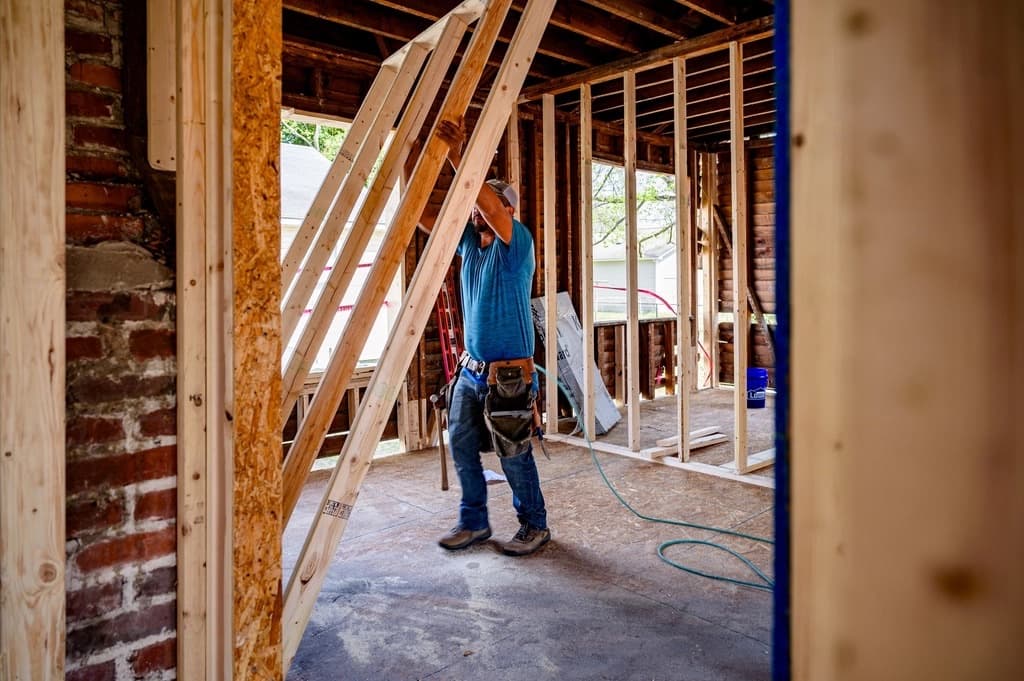 A carpenter setting new wall framing inside a house under renovation